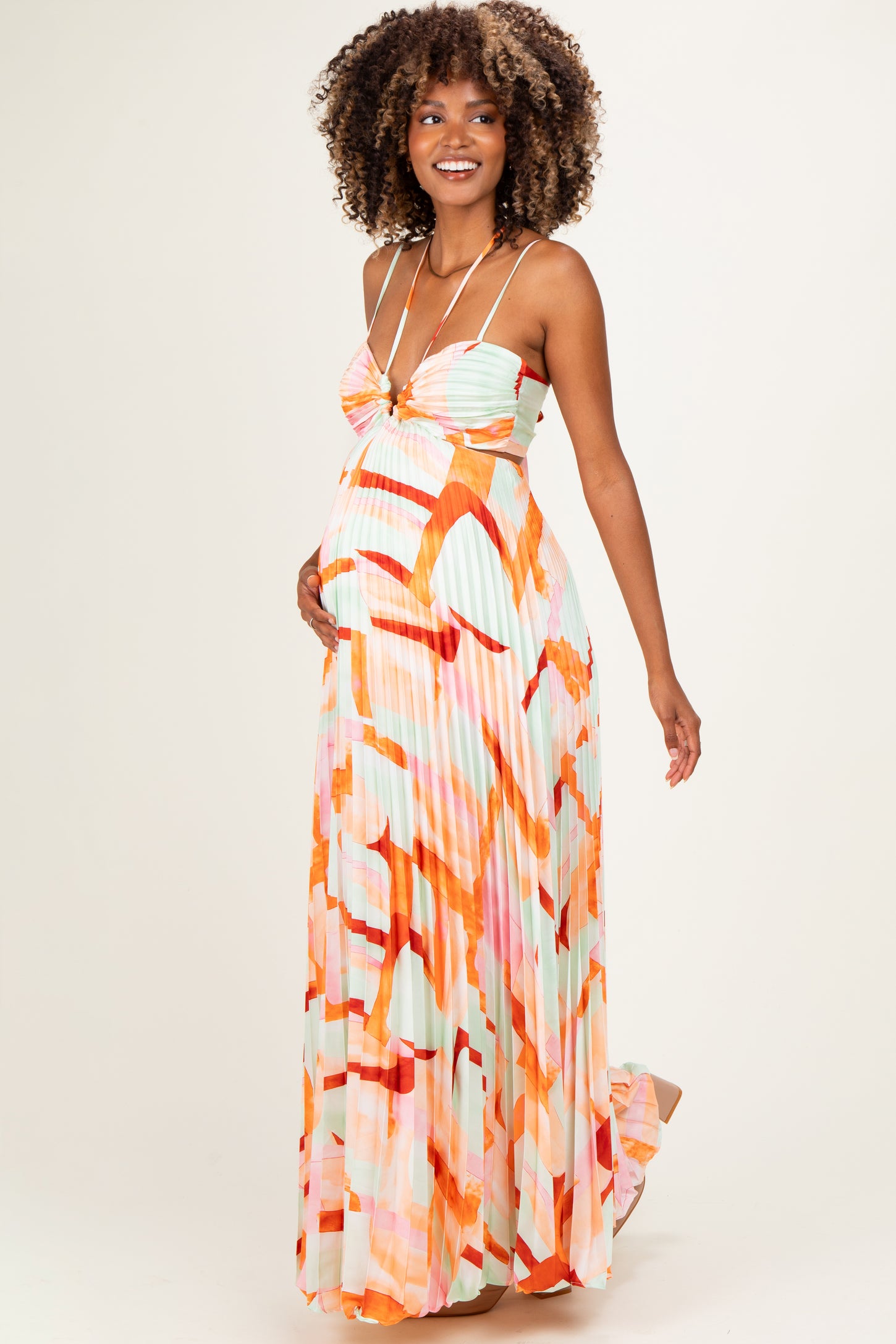 woman wearing a colorful pleated maternity maxi dress with spaghetti straps and a visible baby bump