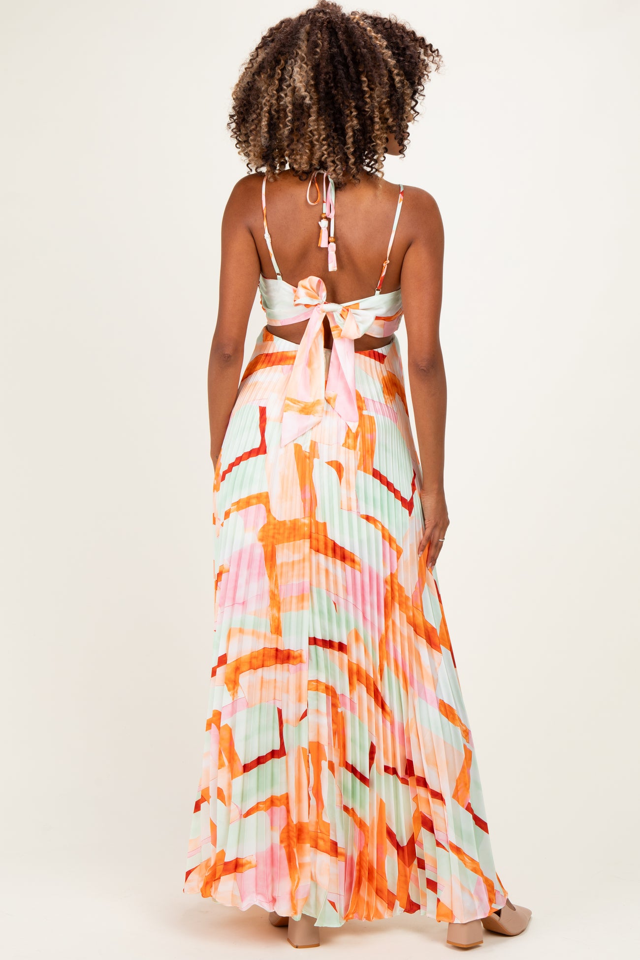woman wearing a colorful patterned maternity maxi dress with a tie back and pleated detailing, no visible baby bump