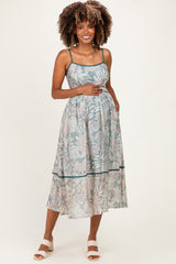 woman wearing a light green floral maternity dress with spaghetti straps and a flowy skirt, holding her baby bump