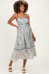 woman wearing a blue floral maternity dress with a flowy skirt and spaghetti straps, showcasing her baby bump
