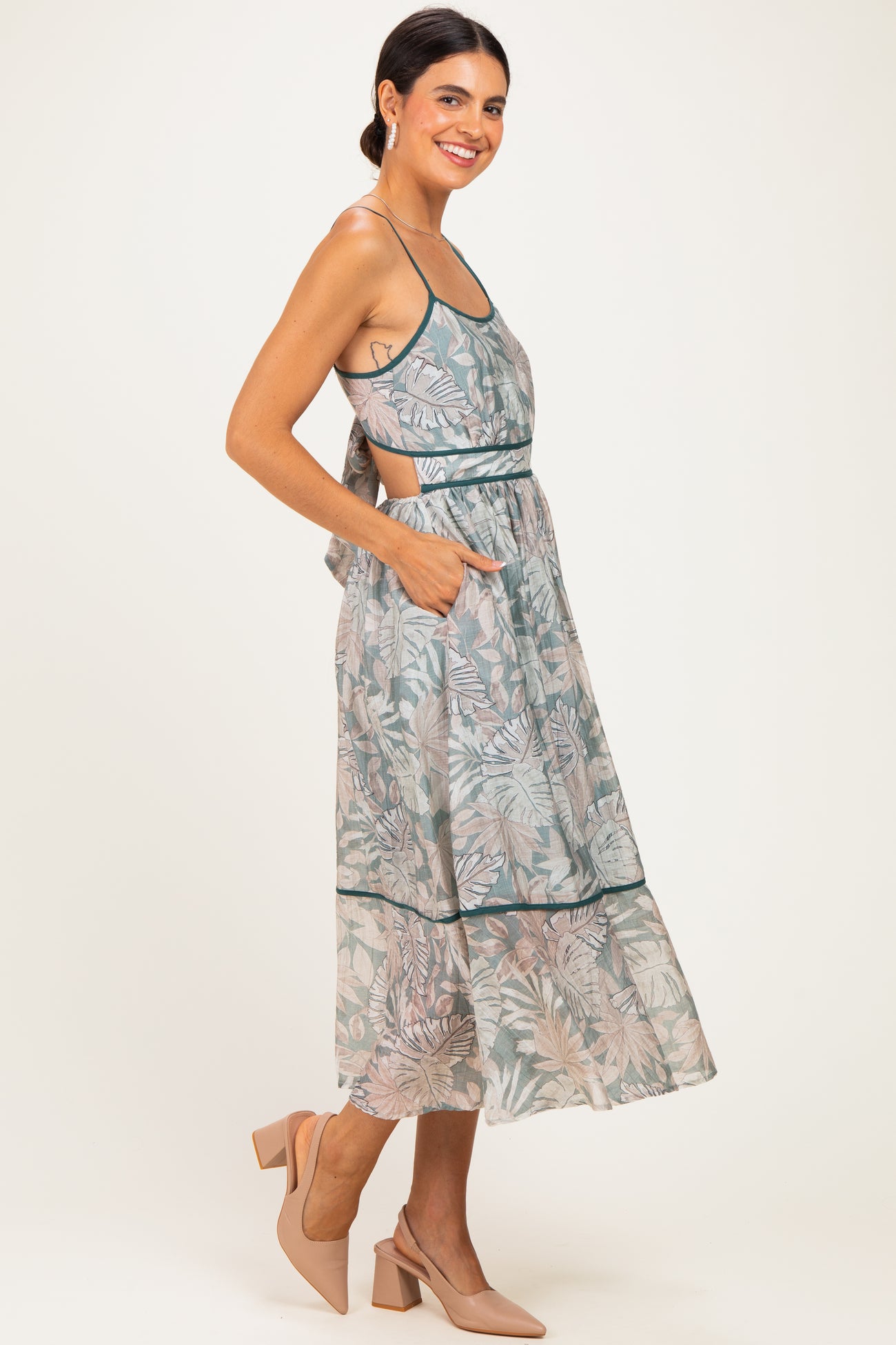 woman wearing a light green floral midi dress with pockets and a back tie detail, paired with beige heels