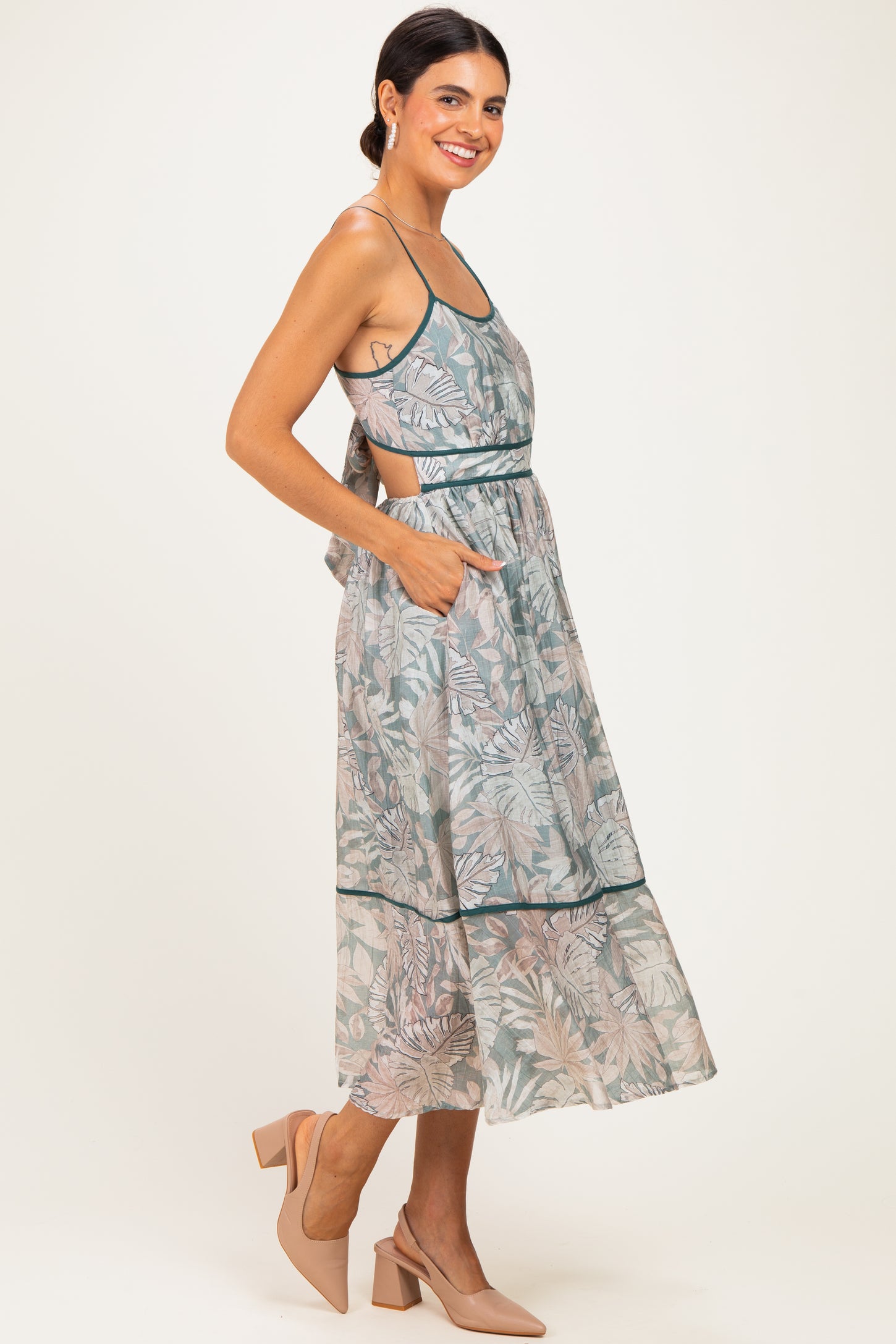 woman wearing a light green floral midi dress with pockets and a back tie detail, paired with beige heels
