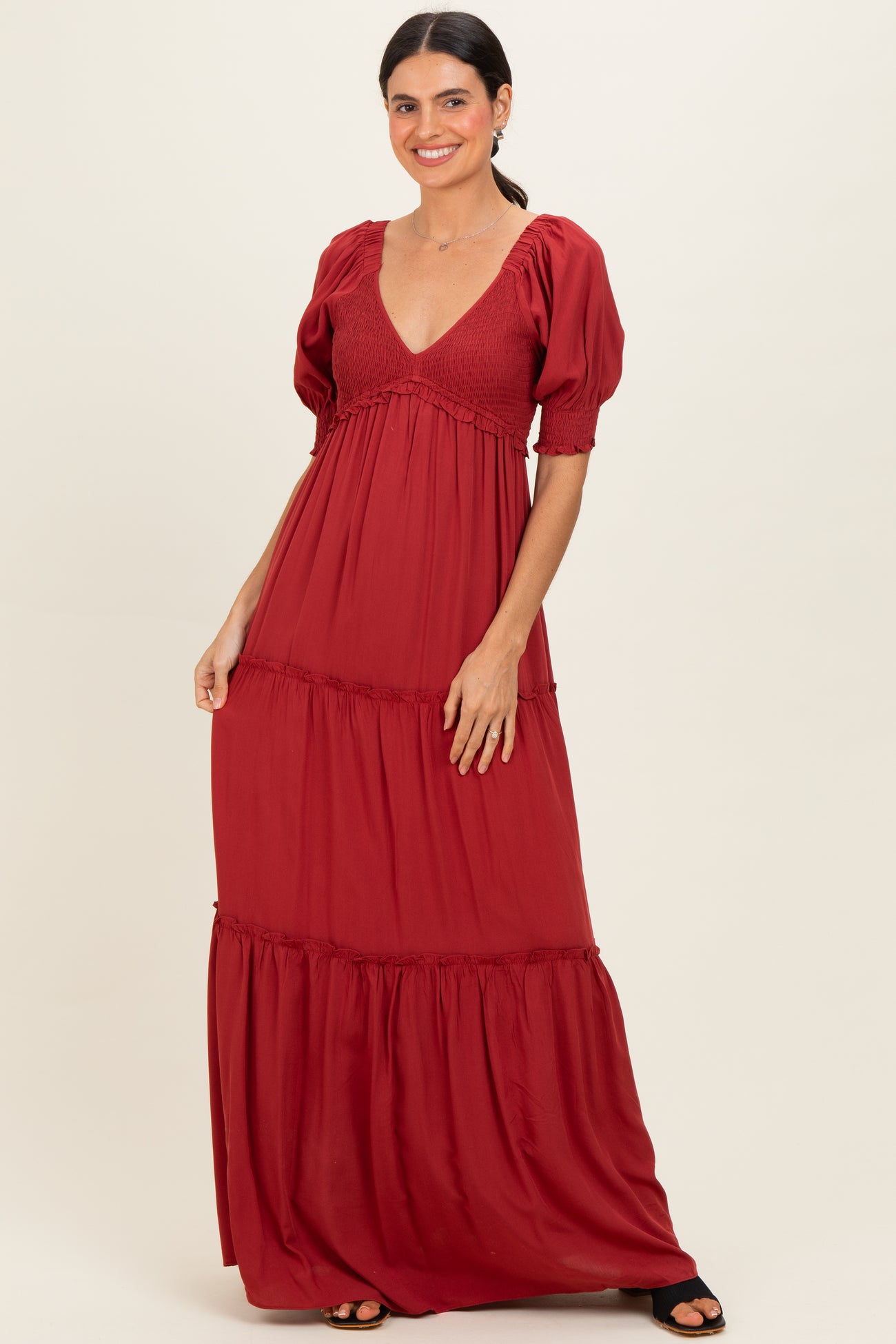 woman wearing a ruby red maxi dress with puff sleeves and tiered ruffles, smiling against a neutral background