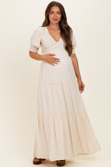 woman wearing a cream maternity maxi dress with puff sleeves and ruffled tiers, holding her baby bump