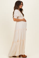 woman wearing a cream maternity maxi dress with puff sleeves and tiered ruffles, gently holding her baby bump