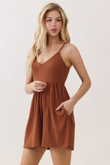 woman wearing a rust-colored spaghetti strap romper with a fitted bodice and loose skirt, featuring side pockets