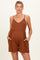 woman wearing a rust-colored sleeveless maternity romper with a v-neck and side pockets, showing her baby bump