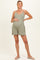 woman wearing a sage green maternity romper with pockets, holding her baby bump and smiling