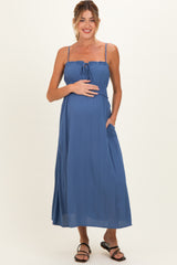 woman wearing a blue sleeveless maternity maxi dress with a tie front and pockets, showcasing her baby bump