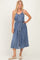 woman wearing a denim midi dress with adjustable straps, a button-down front, and a tied waist belt