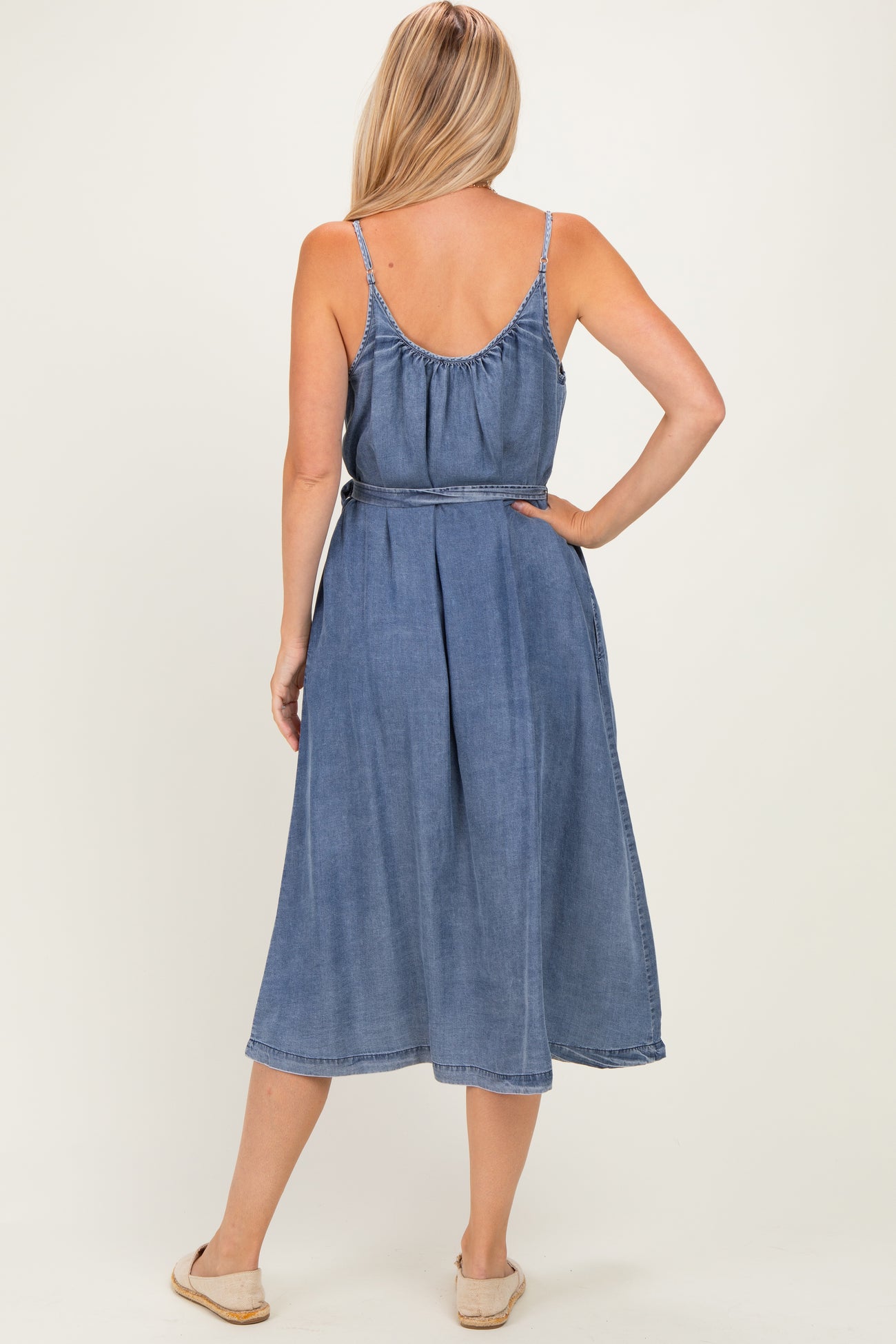 woman wearing a chambray sleeveless midi dress with a belted waist and a flowy skirt from the back