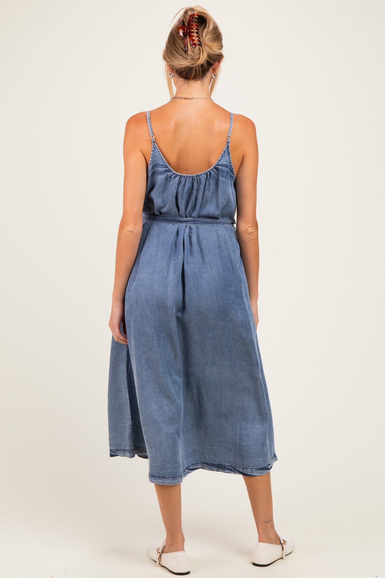 woman wearing a denim maternity dress with a flowy skirt and adjustable straps, showing a baby bump from the back