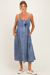 woman wearing a light blue denim maternity dress with a tie waist and pockets, showcasing her baby bump