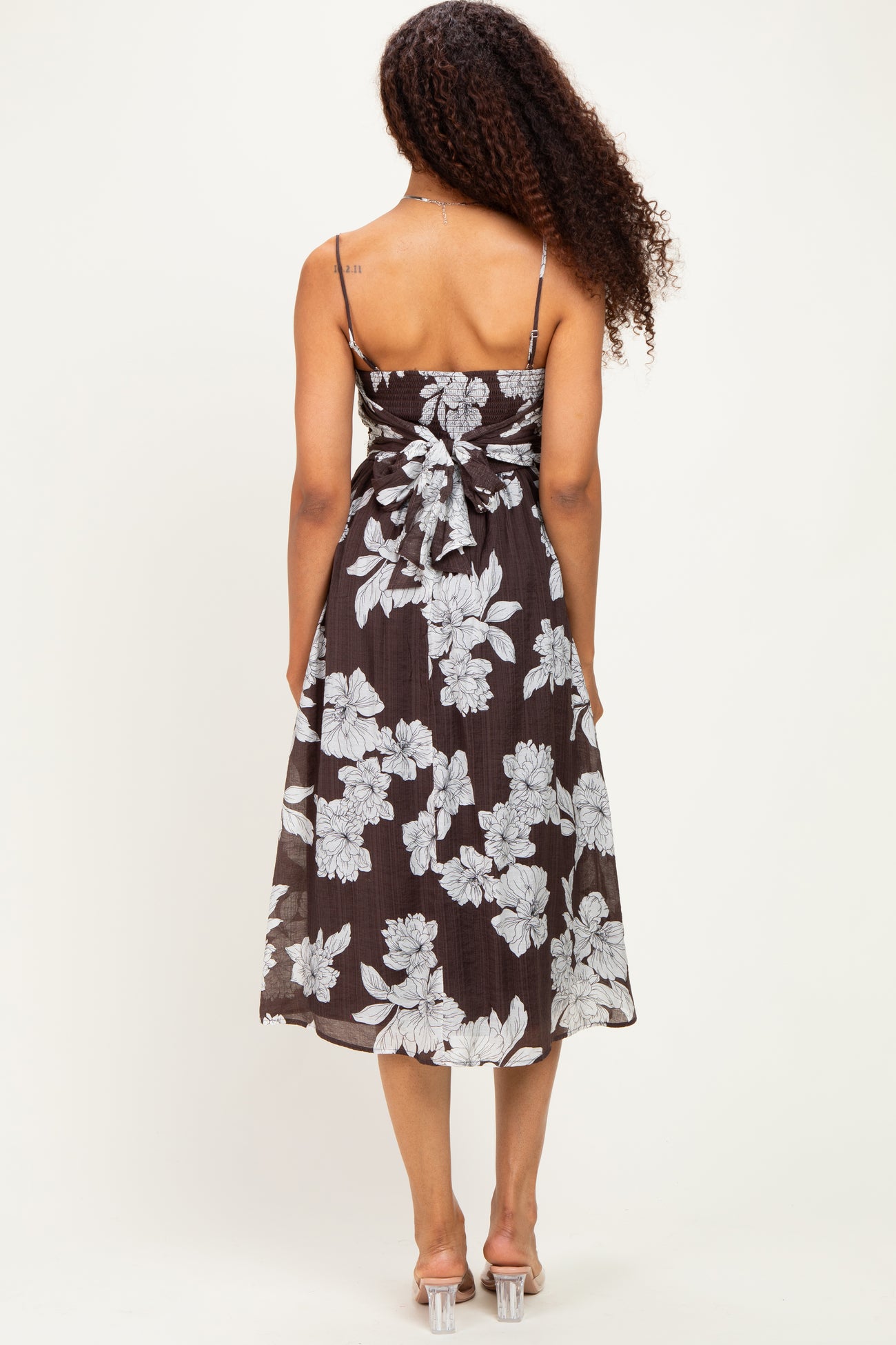 woman wearing a brown floral midi dress with a bow at the back and thin straps
