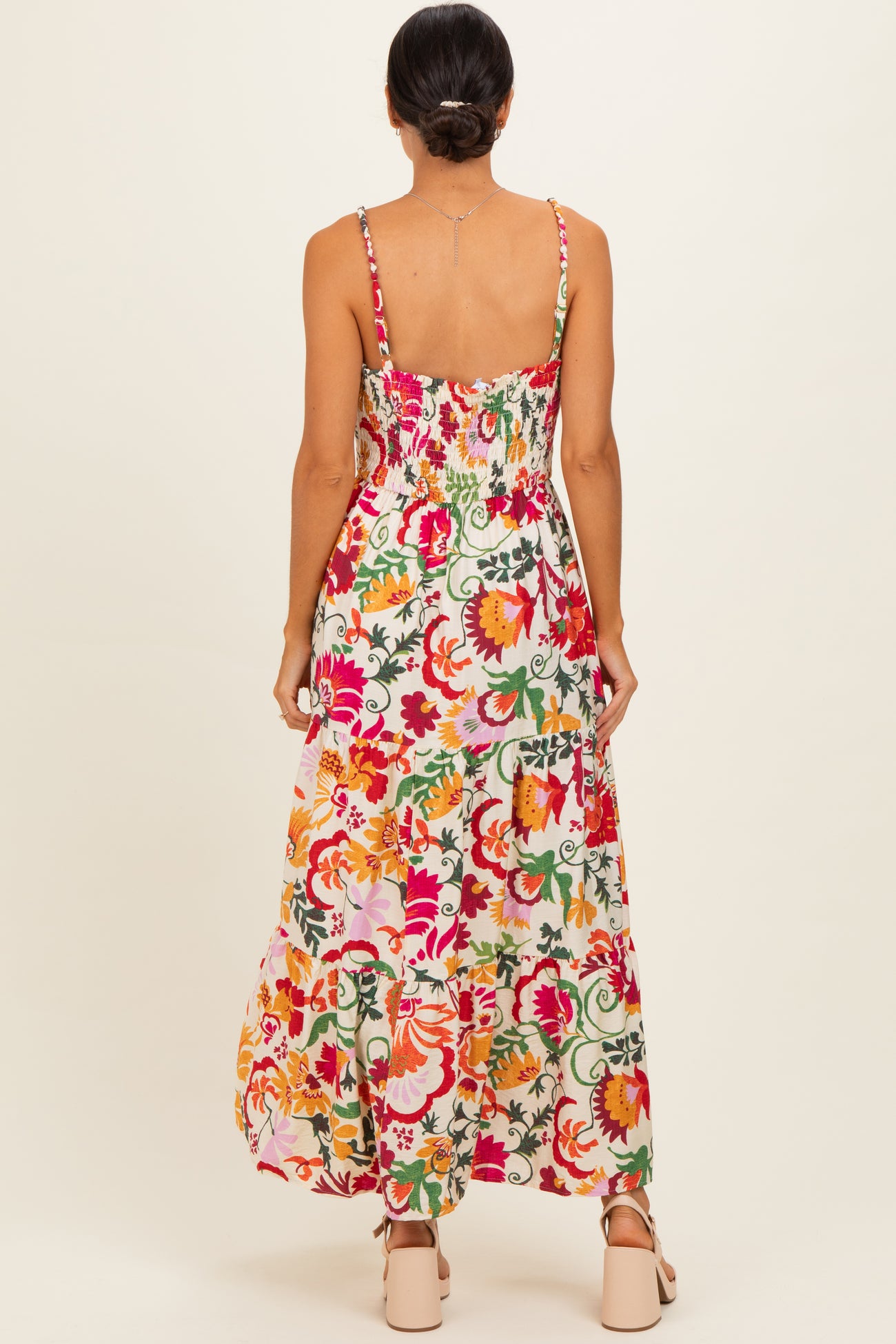 woman wearing a colorful floral maxi dress with adjustable straps and a smocked bodice, shown from the back