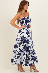 woman wearing a white maxi dress with navy floral print and spaghetti straps, standing in profile