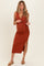 woman wearing a rust-colored ribbed maternity dress with a side slit and a tie detail at the waist, showing her baby bump
