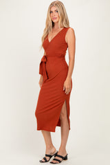 woman wearing a rust-colored sleeveless wrap dress with a tie waist and side slit, styled with black sandals