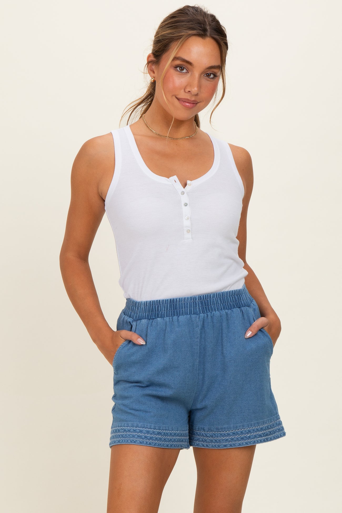 woman wearing a white button-up tank top and blue drawstring shorts with pockets and decorative stitching