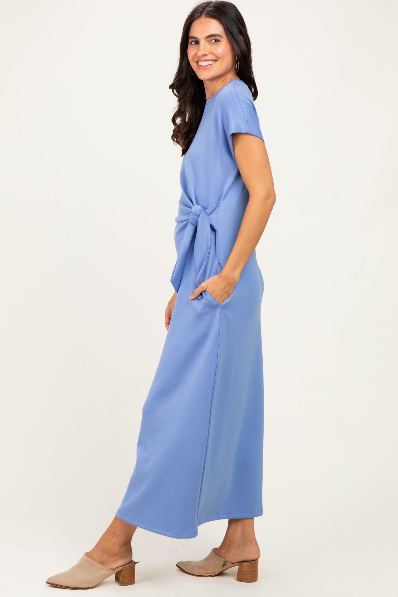woman wearing a light blue maxi dress with short sleeves and a knot detail at the waist, paired with beige mules
