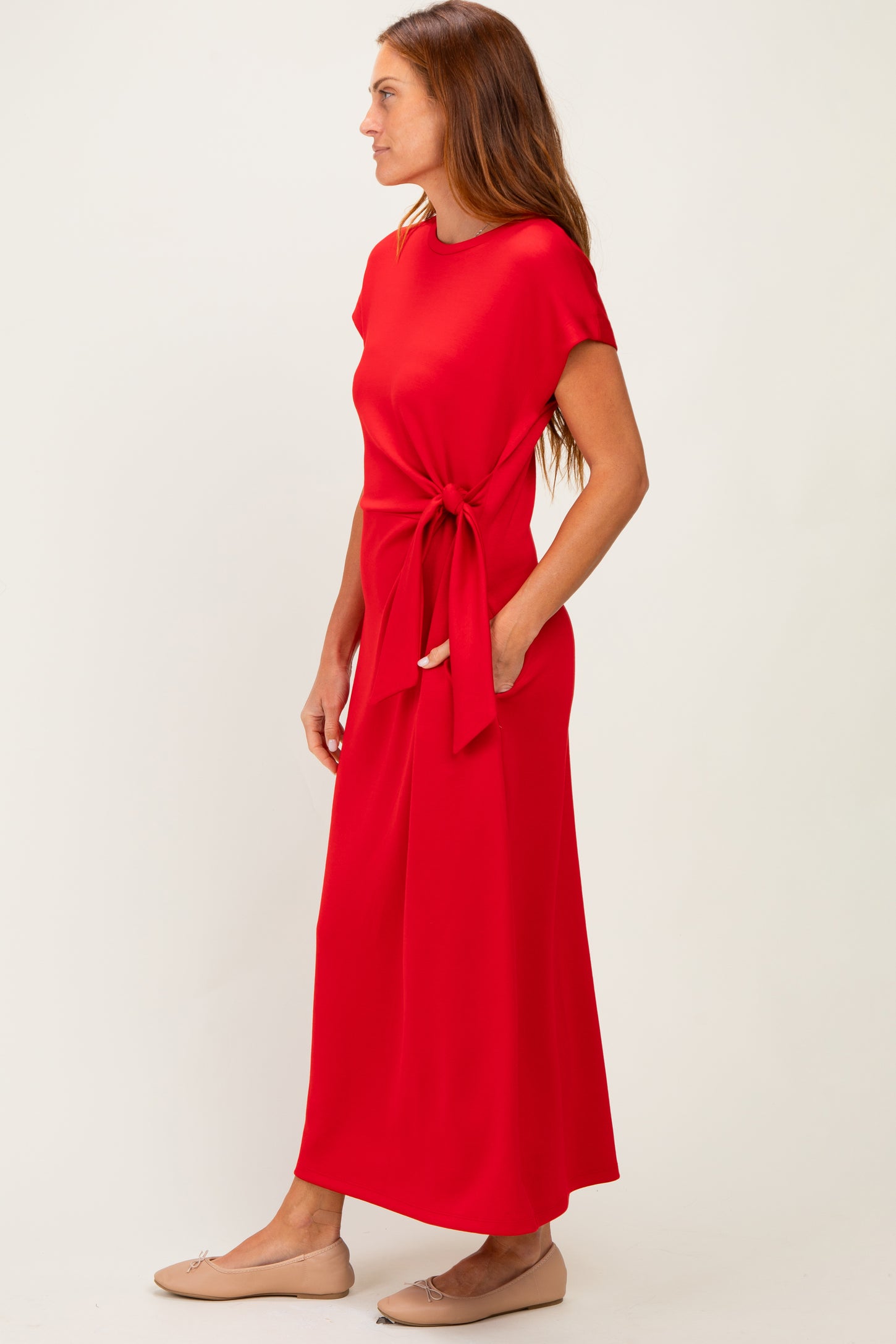 woman wearing a red maxi dress with a tied waist detail and short sleeves, paired with flat shoes