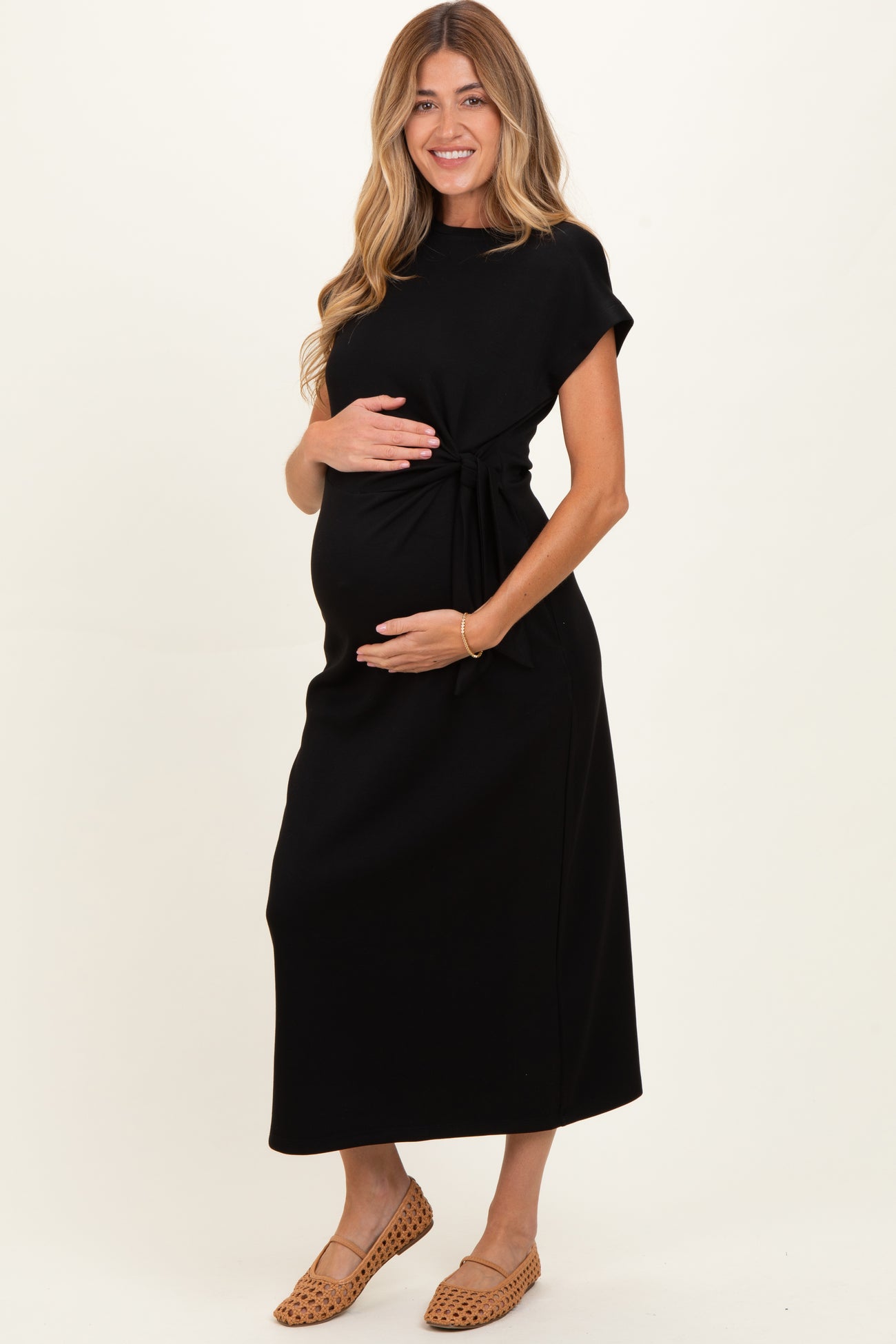 woman wearing a black maternity dress with a tie waist detail and holding her baby bump