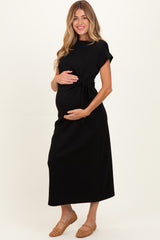 woman wearing a black maternity dress with a tie waist detail and holding her baby bump