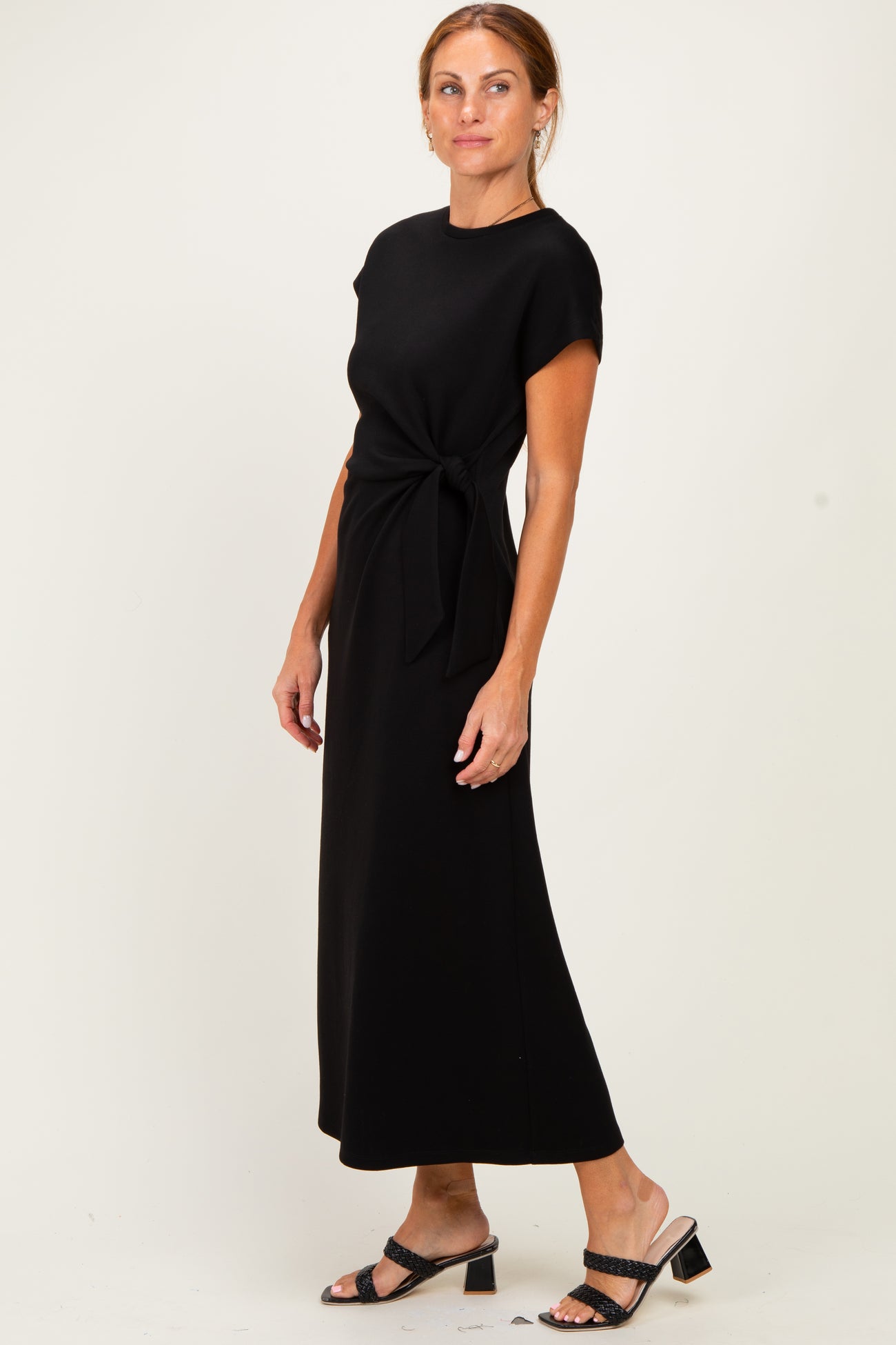 woman wearing a black cap sleeve maxi dress with a tie detail at the waist and black heeled sandals