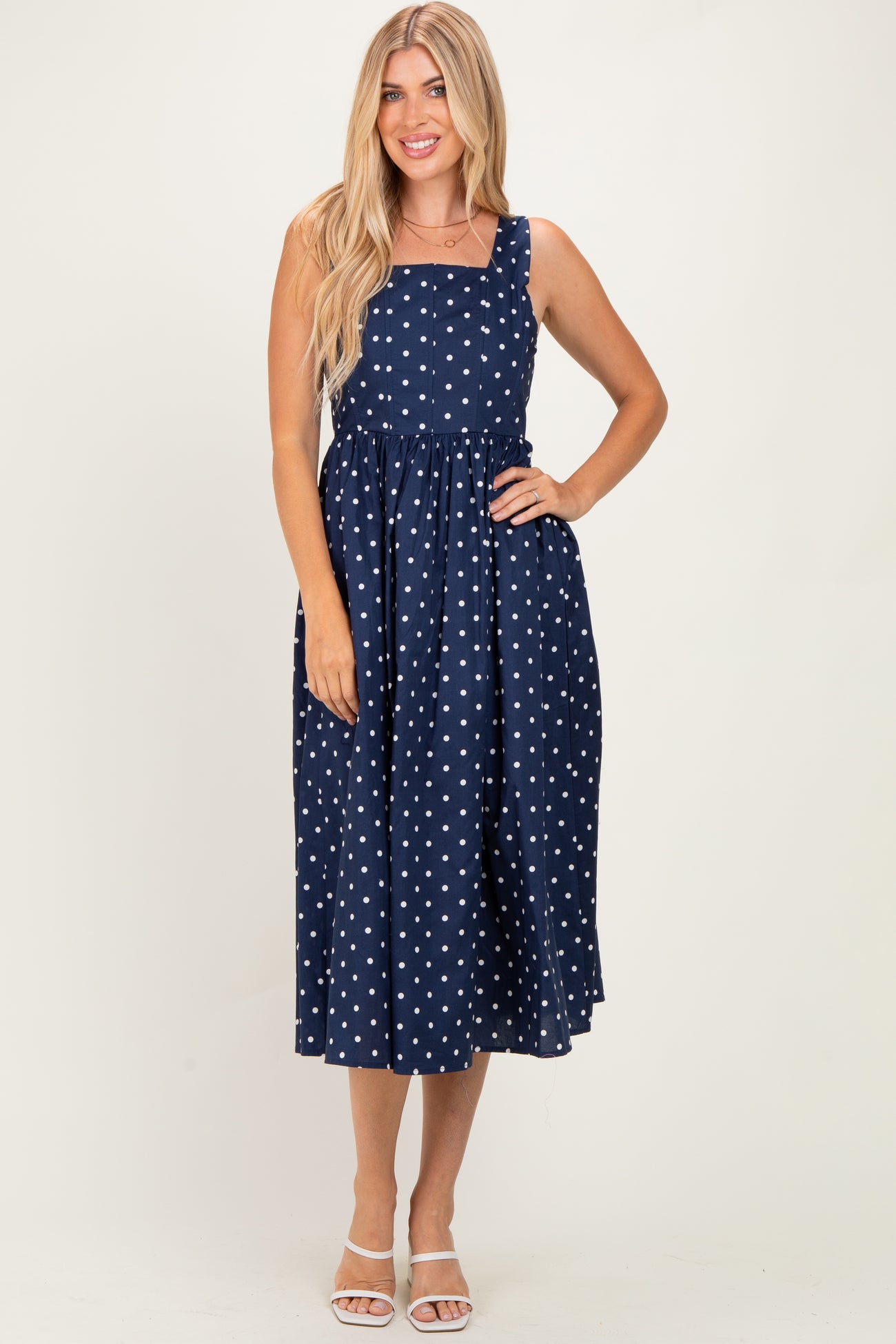 woman wearing a navy blue polka dot midi dress with a square neckline and adjustable straps