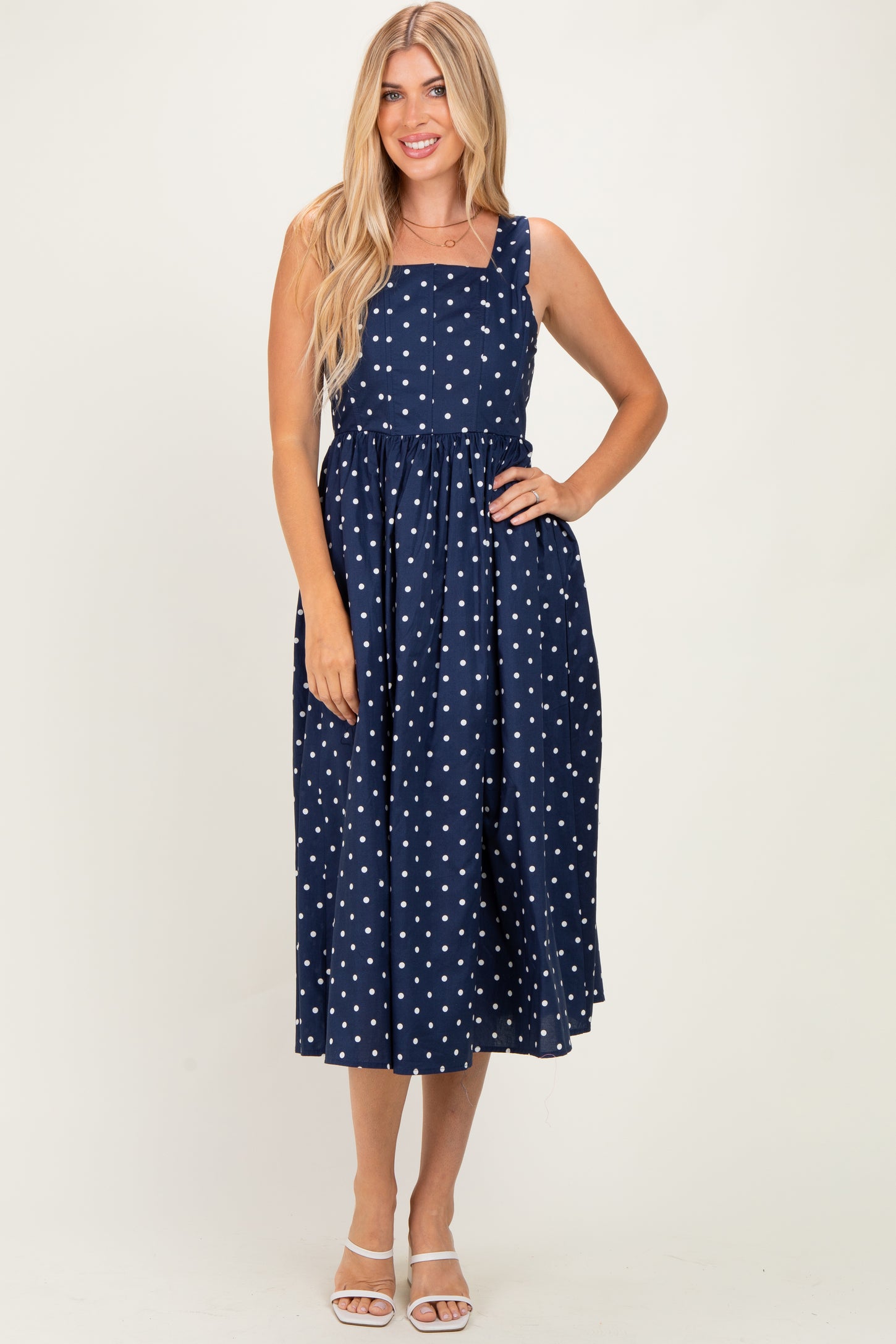 woman wearing a navy blue polka dot midi dress with a square neckline and adjustable straps