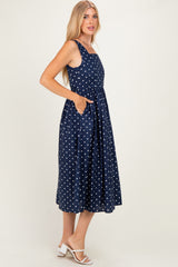 woman wearing a navy blue midi dress with white polka dots and side pockets, styled with strappy white sandals