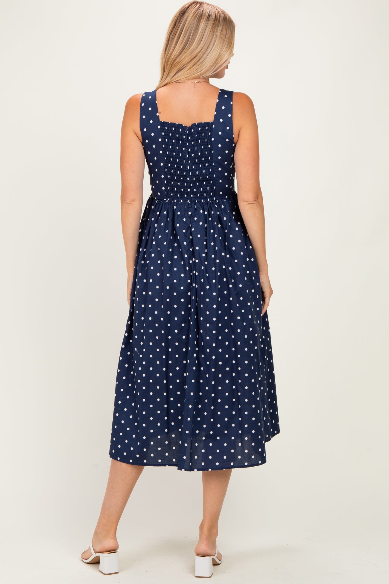 woman wearing a navy blue polka dot sundress with a smocked back and a midi length, showing the back view