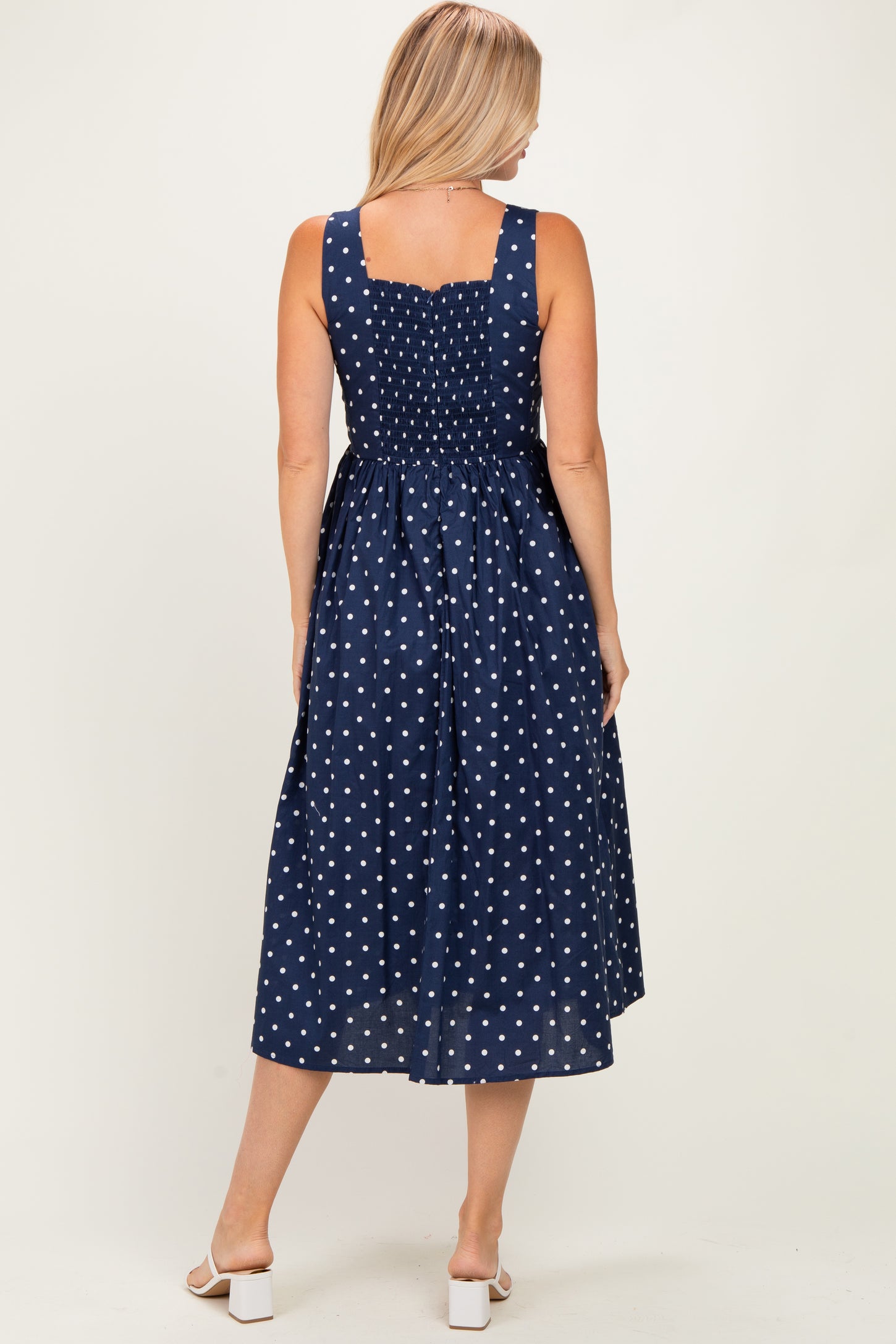 woman wearing a navy blue polka dot sundress with a smocked back and a midi length, showing the back view