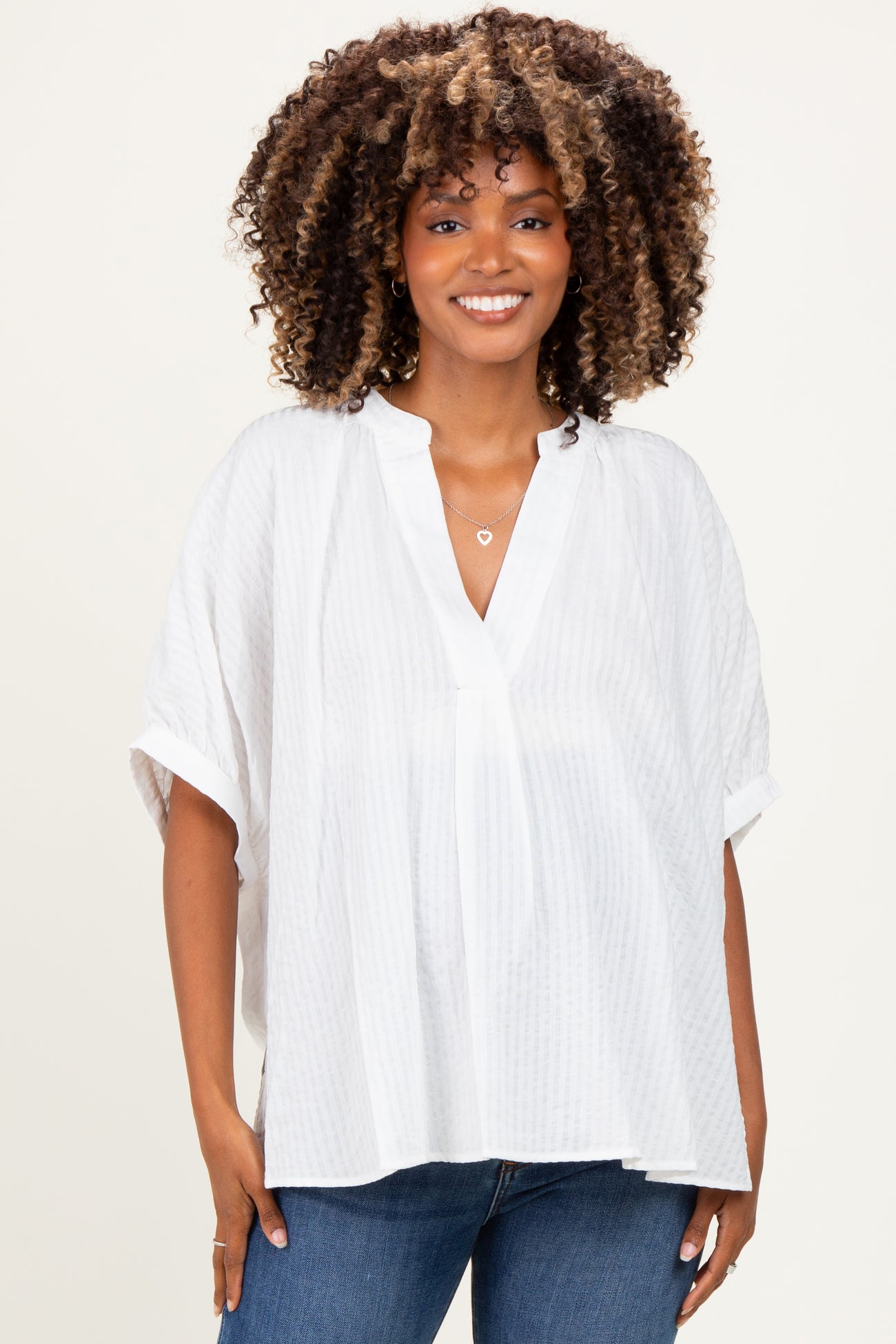 woman wearing a white oversized maternity top with a v-neck and short sleeves, smiling at the camera