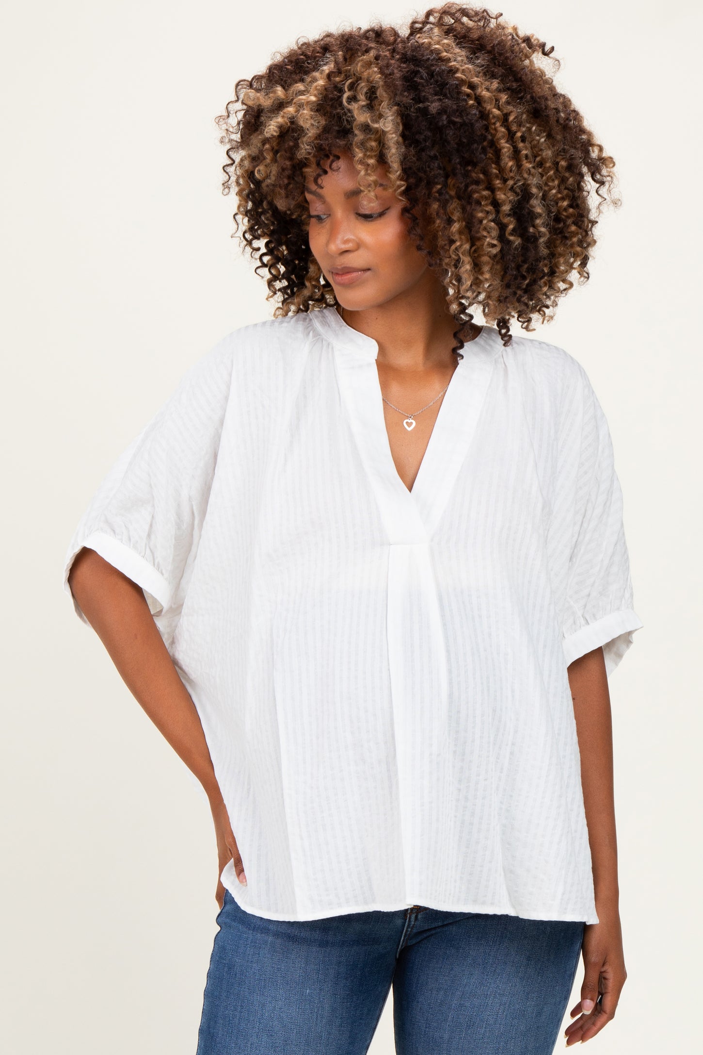 woman wearing a white maternity top with a v-neck and short sleeves, styled with denim jeans