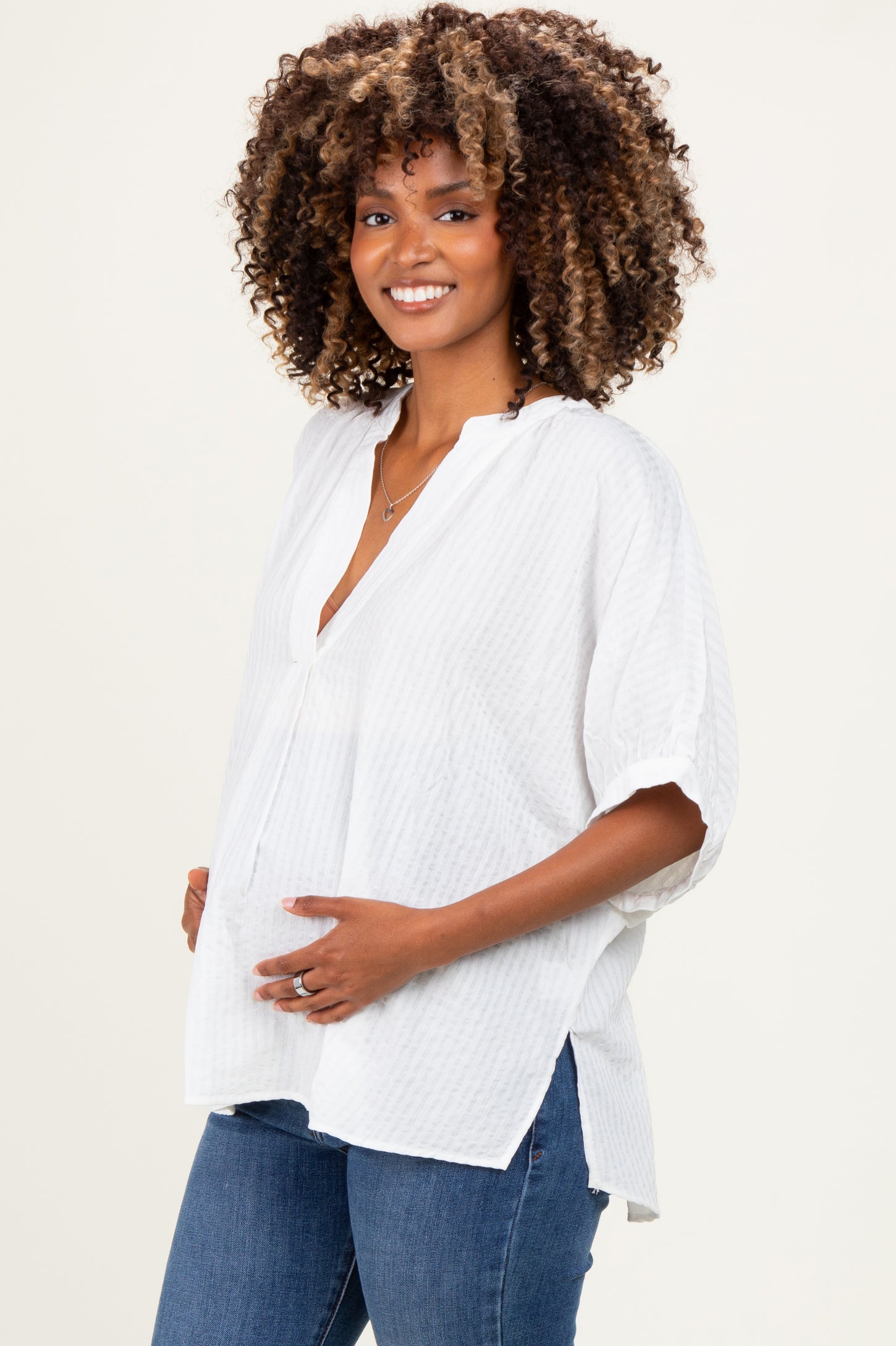 woman wearing a white short sleeve maternity blouse with a v-neck and holding her baby bump