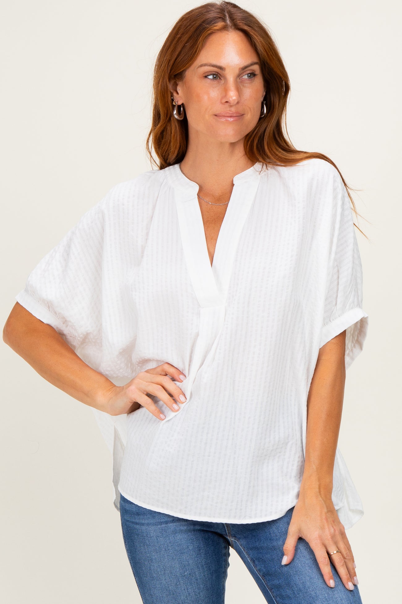 woman wearing a white short sleeve blouse with a v-neck and loose fit paired with blue jeans