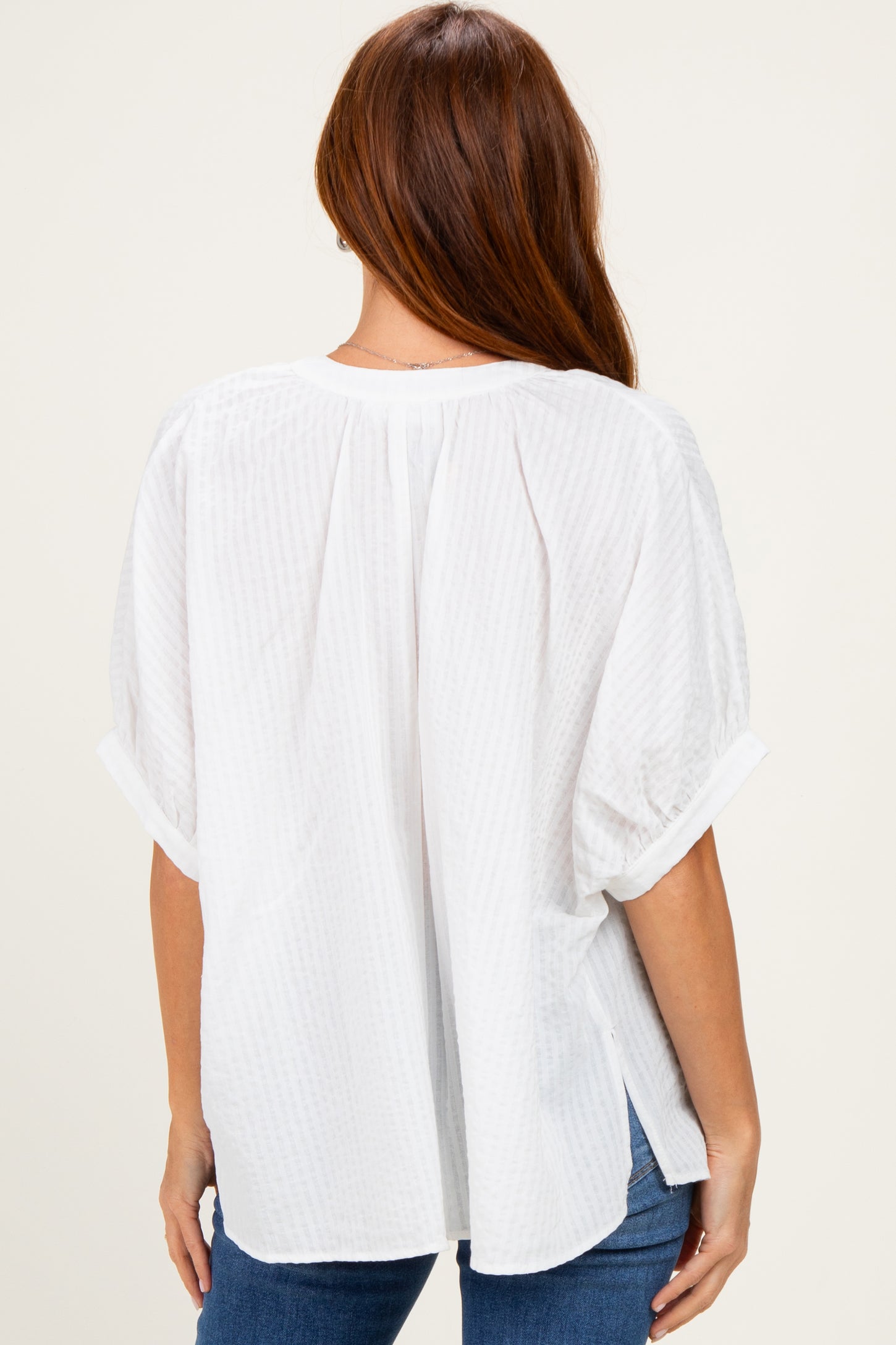 woman wearing a white short sleeve blouse with a textured pattern and a relaxed fit, seen from the back