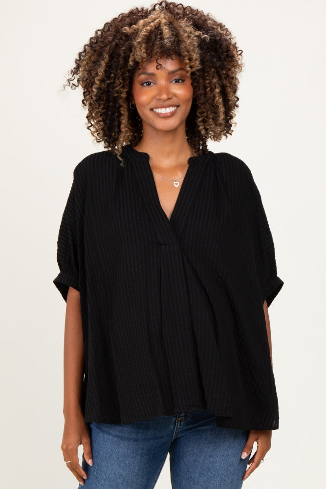 woman wearing a black maternity top with a relaxed fit and short sleeves, smiling at the camera