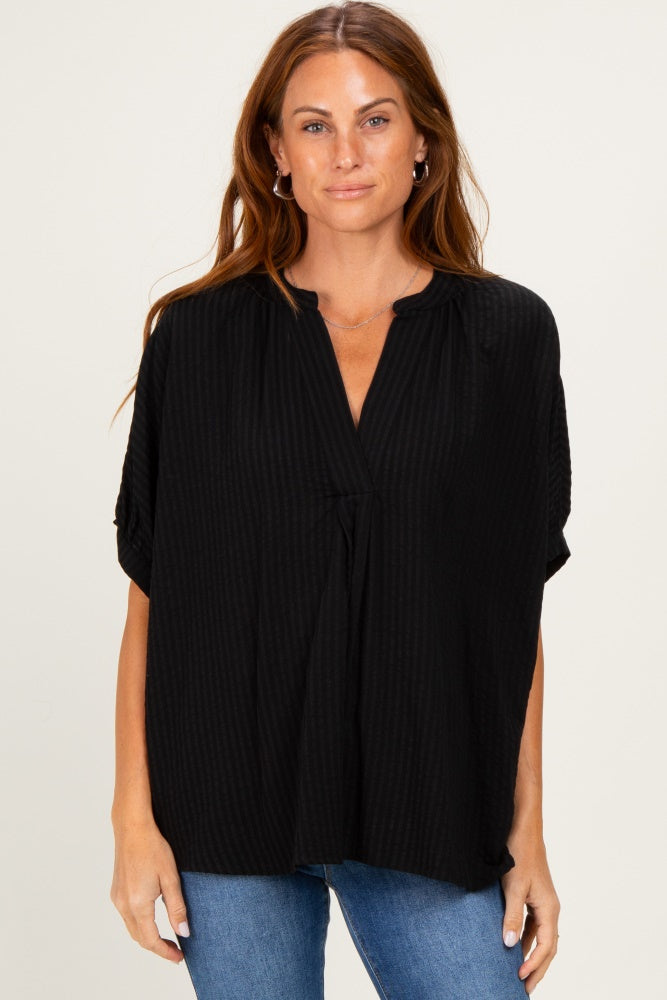 woman wearing a black loose-fit striped blouse with a v-neck and short sleeves, paired with blue jeans