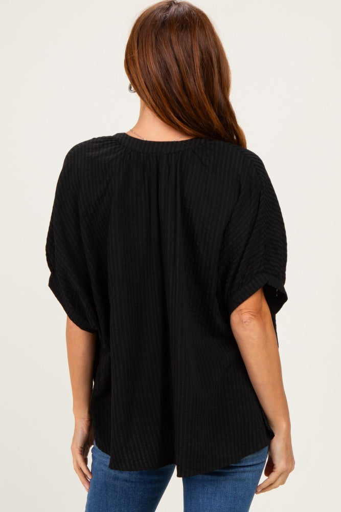 woman wearing a black short sleeve top with a textured pattern and relaxed fit, showing the back view