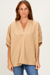 woman wearing a light brown short sleeve top with a v-neck and relaxed fit, paired with blue jeans