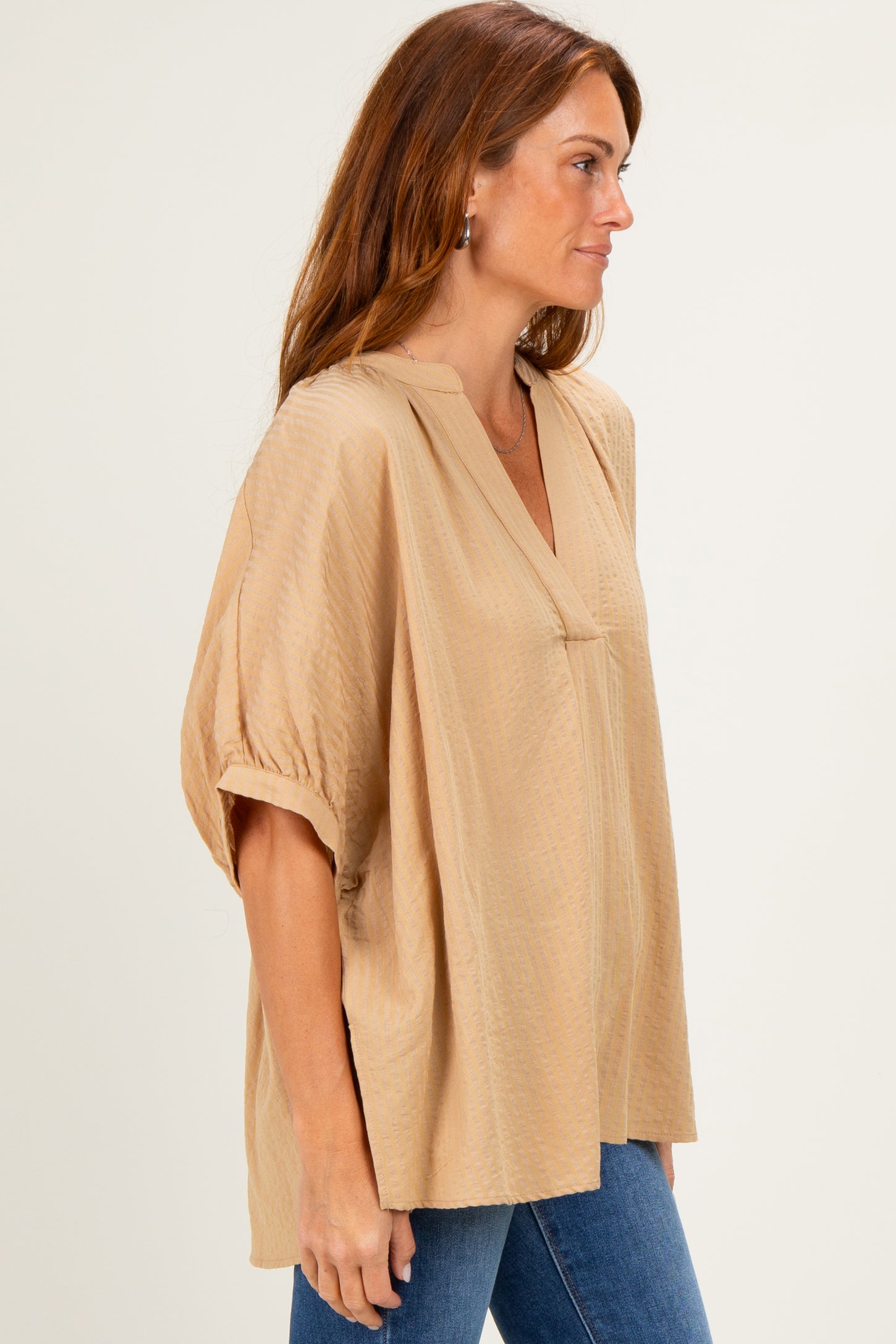 woman wearing a beige short sleeve blouse with a v-neck and relaxed fit paired with blue jeans