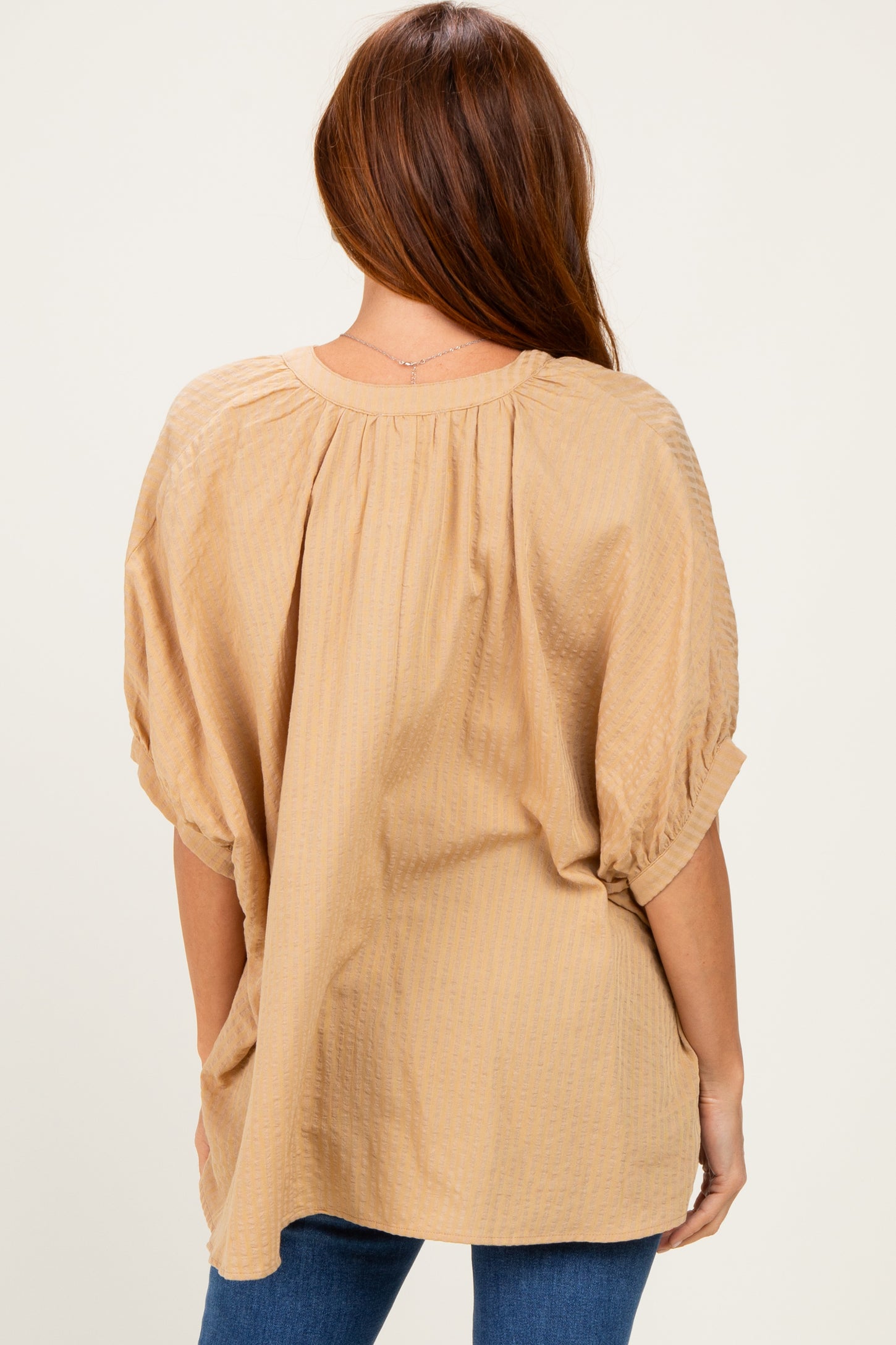 woman wearing a light tan oversized blouse with gathered back detail and rolled sleeves, viewed from behind