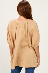 woman wearing a light tan oversized blouse with gathered back detail and rolled sleeves, viewed from behind