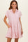 woman wearing a light pink maternity button-up dress with short sleeves and a tiered ruffle hem