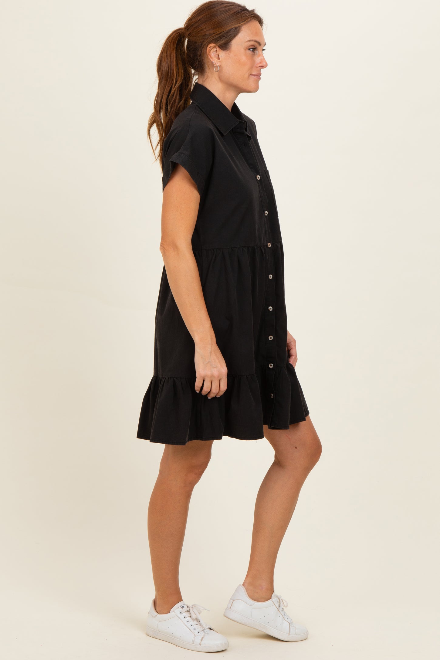 woman wearing a black short sleeve shirt dress with a button front and ruffle hem, styled with white sneakers
