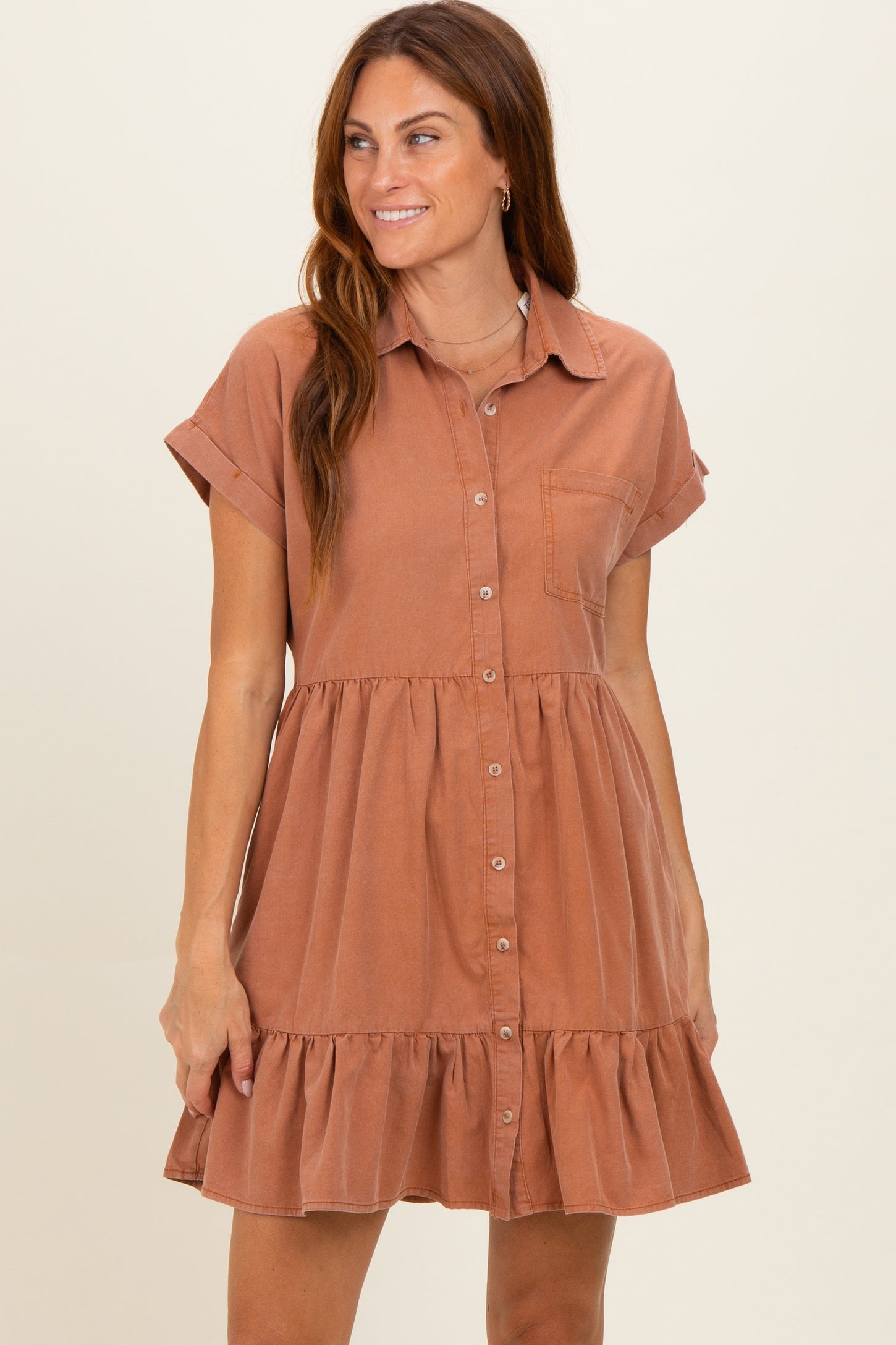 woman wearing a rust-colored short sleeve button-up maternity dress with a tiered ruffle hem and front pocket