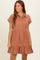 woman wearing a rust-colored short sleeve button-up maternity dress with a tiered ruffle hem and front pocket