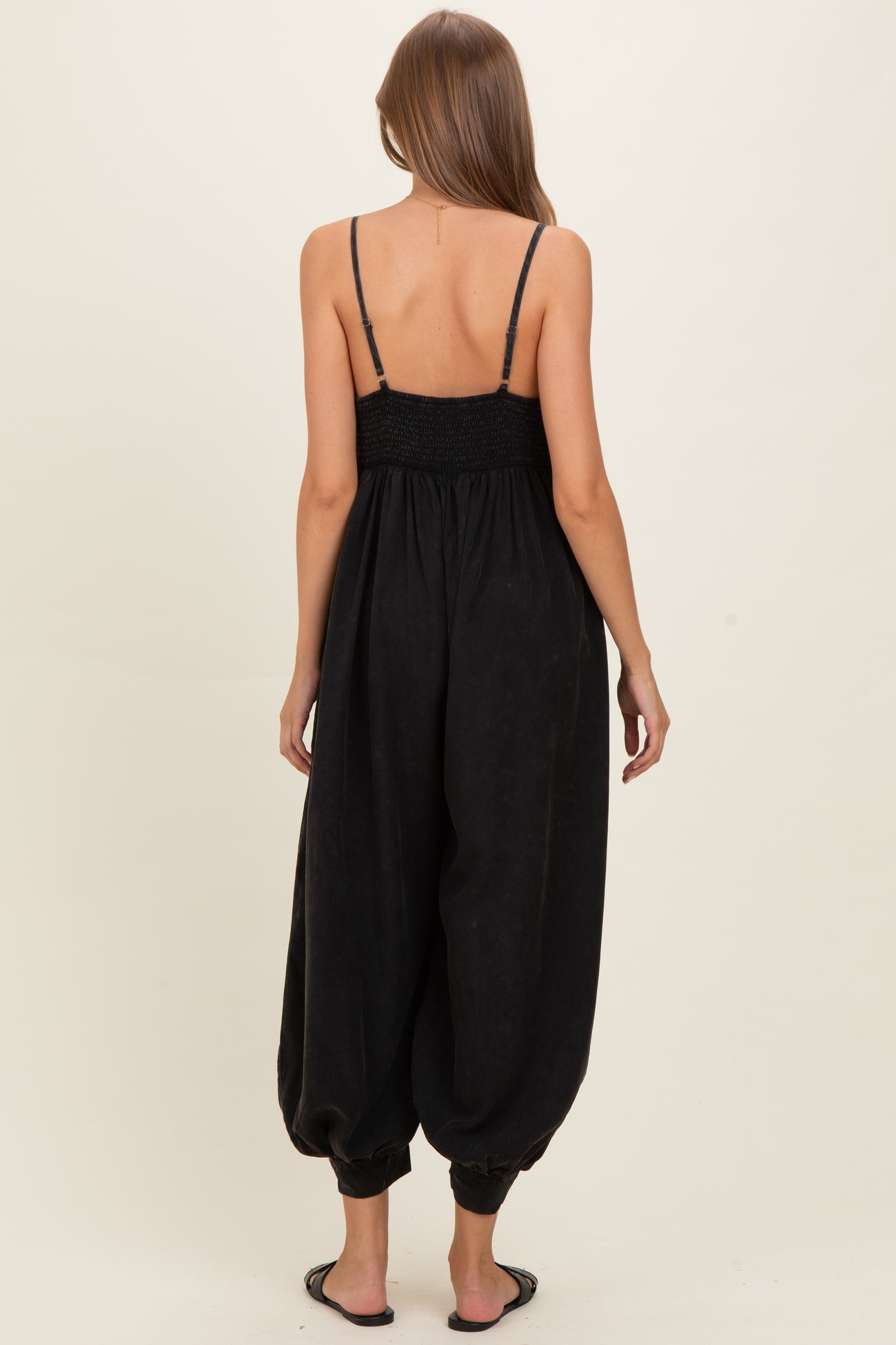woman wearing a black maternity jumpsuit with a smocked back and loose, tapered legs